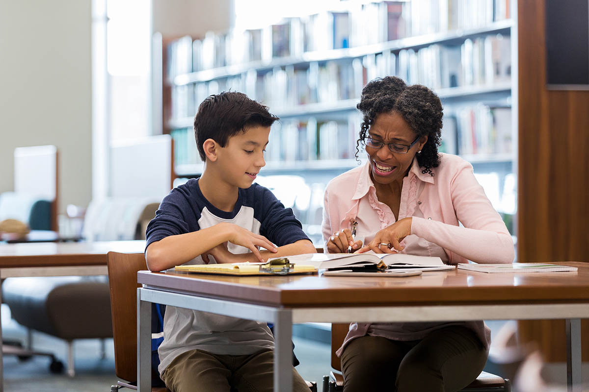 Middle school age boy reads with mentor in library